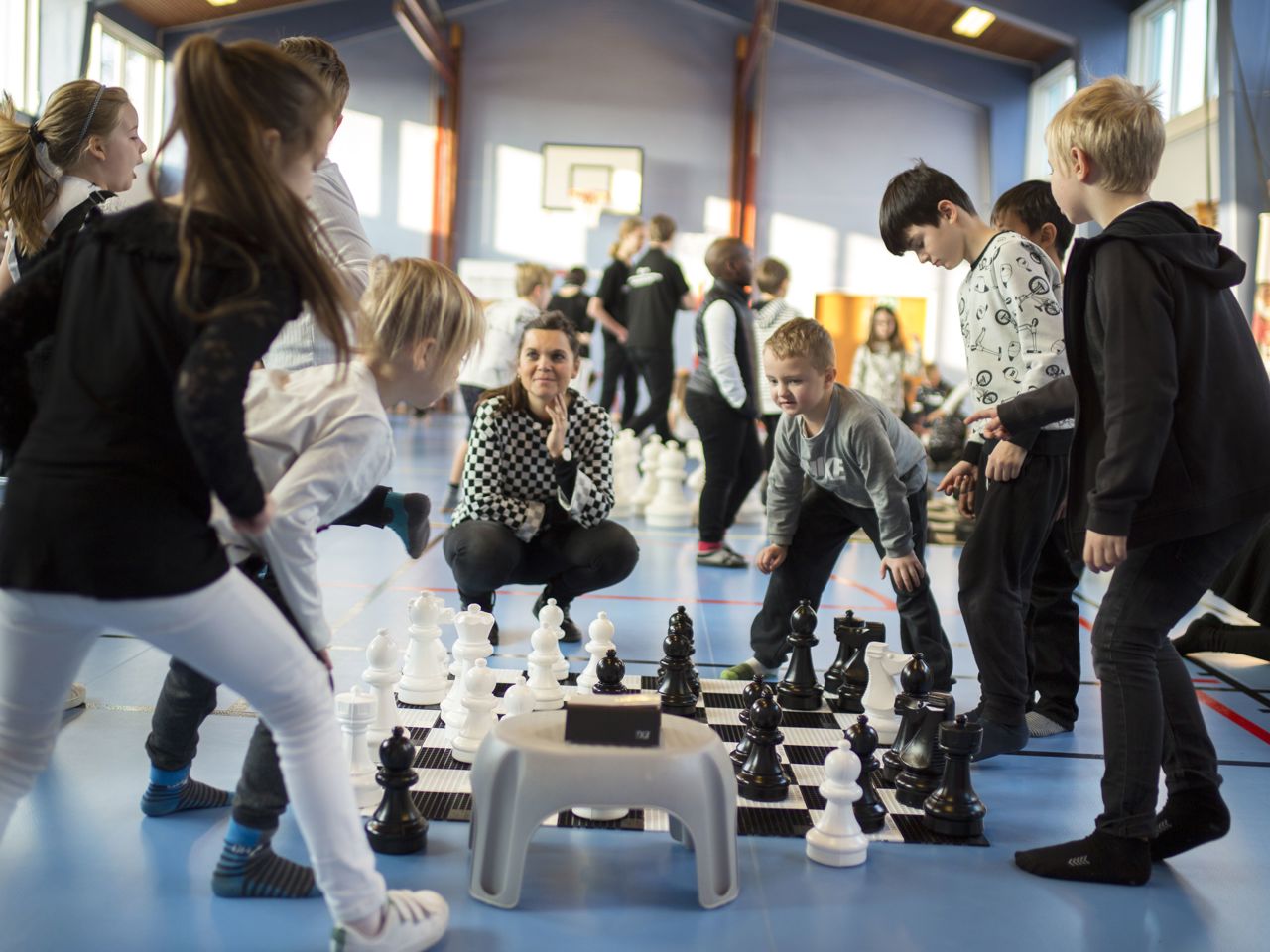 otte elever på mellemtrinnet står om et skakbræt på gulvet